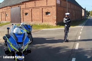 policyjny motocyklista stoi przy drodze i kontroluje prędkość