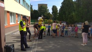 Na zdjęciu widać jak policjanci oraz człowiek maskotka rozdają dzieciom kamizelki odblaskowe na placu szkoły.