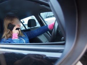 Zdjęcie przedstawia kierowce, który prowadząc samochód jednocześnie używa telefonu komórkowego.