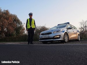 Zdjęcie przedstawia policjanta stojącego z lizakiem przy drodze obok radiowozu.