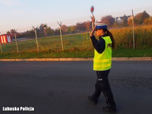 Zdjęcie ukazuje policjantkę z lizakiem, która stojąc na drodze wykonuje gest zatrzymania nadjeżdżającego pojazdu