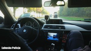 Zdjęcie przedstawia wnętrze jadącego radiowozu z dwoma policjantami.