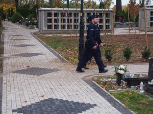 Na zdjęciu widoczni są dwaj policjanci poruszający się na terenie cmentarza.