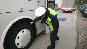 Na zdjęciu funkcjonariusz Inspekcji Transportu Drogowego kontroluje stan ogumienia autobusu.