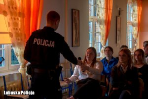Zdjęcie przedstawia policjanta rozmawiającego z młodzieżą, który przekazuje mikrofon uczennicy chcącej się wypowiedzieć podczas debaty.