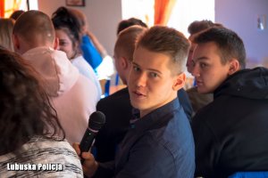Zdjęcie przedstawia młodzież uczestniczącą w debacie. Jeden z chłopaków wypowiada się do mikrofonu.