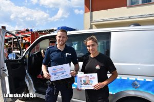 Policjant i Pani Strażak przy radiowozie trzymają napisy akcji promujących bezpieczeństwo
