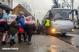 policjanci stojący przy wejściu do autobusu, do którego wchodzą dzieci