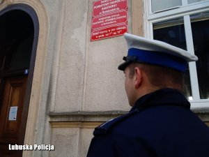 policjant stojący tyłem, w tle budynek SANEPID-u