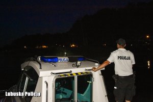 Policjant na łodzi sprawdza linie brzegową jeziora przy ośrodku w nocy