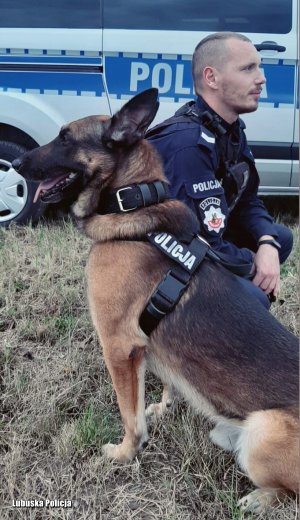 Policjant i pies policyjny na tle radiowozu