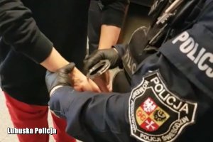 policjant zakłada kajdanki na ręce trzymane z tyłu zatrzymanej kobiecie