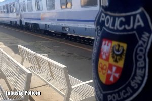rękaw policjanta wraz z naszywką świebodzińskiej policji a w tle odjeżdżający pociąg