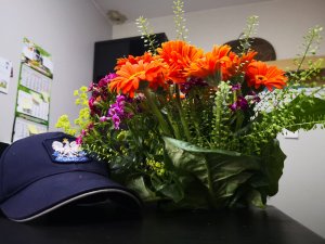 Na biurku leży bukiet kwiatów oraz policyjna czapka