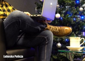 Nogi siedzącego mężczyzny, na kolanach ma laptopa, w tle choinka.
