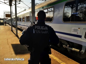 Umundurowany policjant na stacji, w tle odjeżdżający pociąg