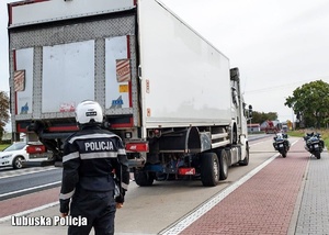 Policjant w kasku motocyklowym, za nim ciężarówka stojąca na drugiej.