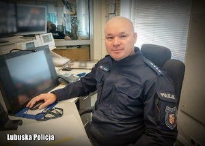 Policjant siedzący za biurkiem, obok monitory